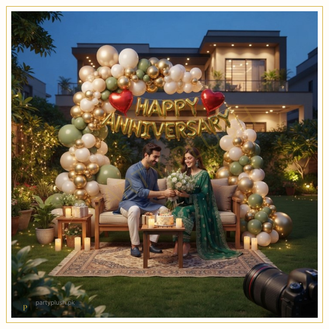 Luxury garden anniversary decoration with organic balloon arch, gold Happy Anniversary foil balloons, red heart foil balloons, fairy lights and romantic outdoor setup.
