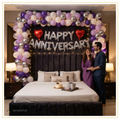 Royal bedroom anniversary decoration with premium balloon garland, gold Happy Anniversary foil balloons, red heart foil balloons and warm fairy lights.